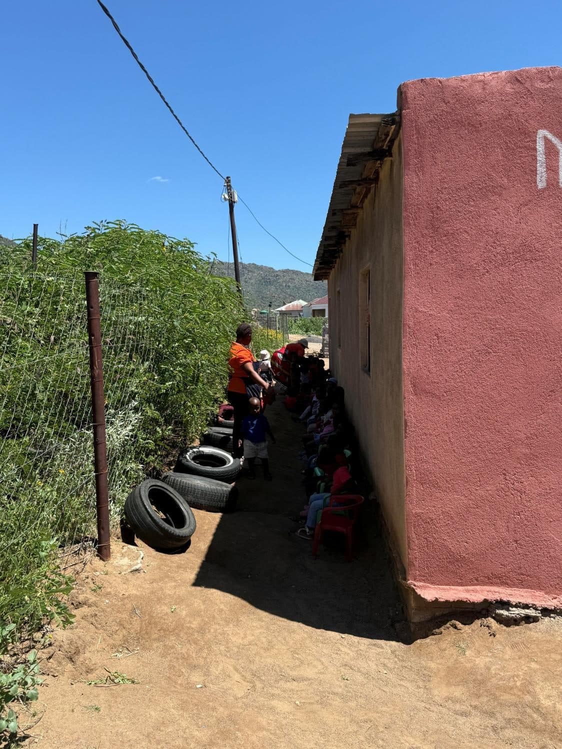 Young children seated on tyres for a class held outdoors beside a building.
