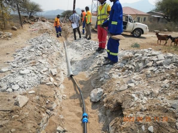 Workers installing a water pipeline through rocky ground.